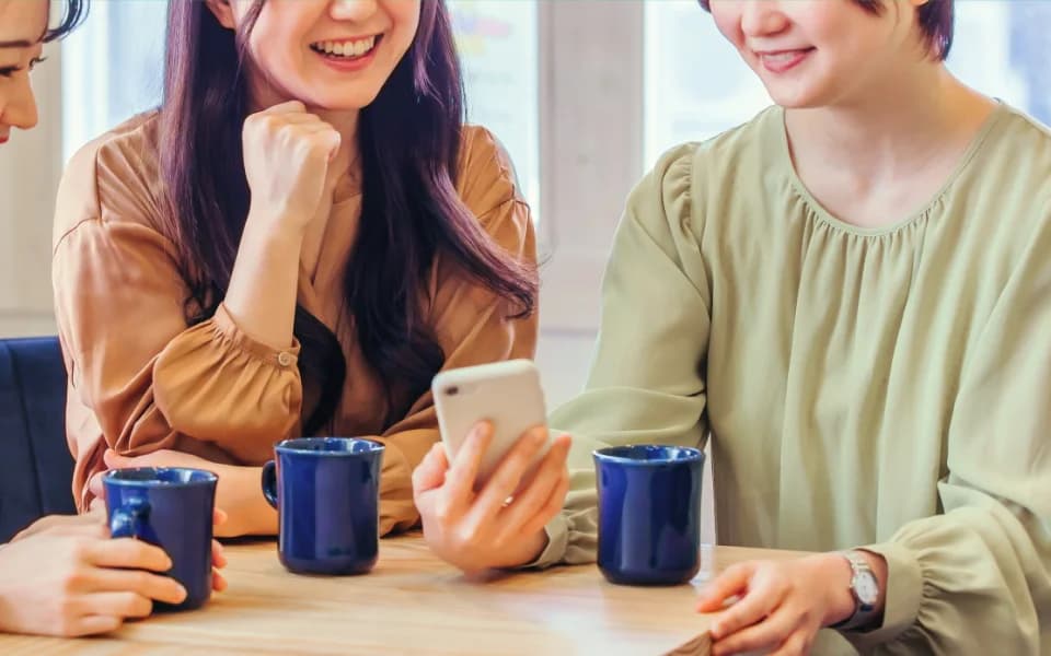 カフェのテーブルでスマートフォンを見ながら会話している3人